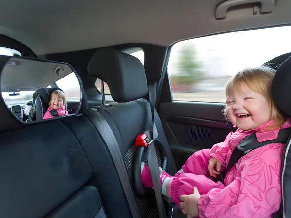 The baby girl is looking in the mirror on the back of the car seat and smiling