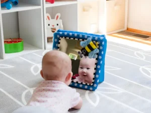 The baby was curiously studying their own reflection in the toy mirror