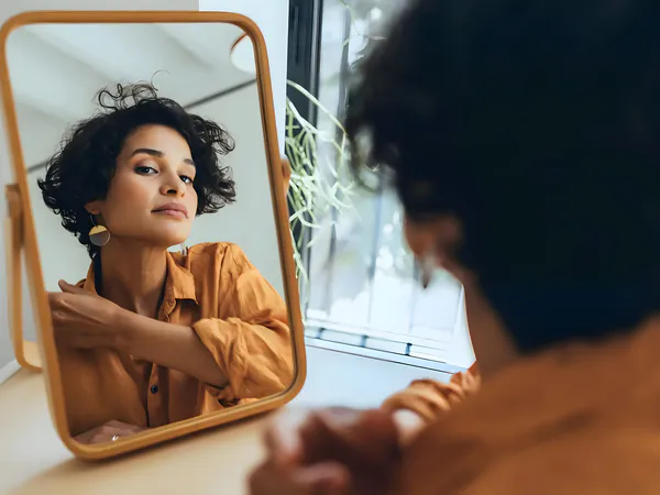 The woman is looking at herself in a standing vanity mirror