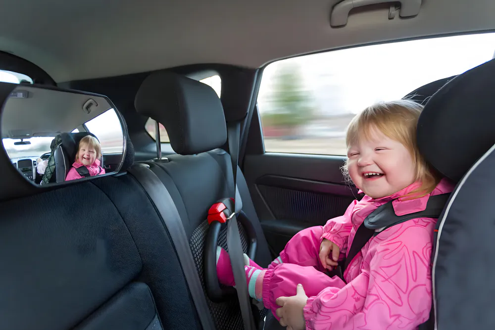 The baby girl looks at the mirror on the back of the car seat and laughs happily