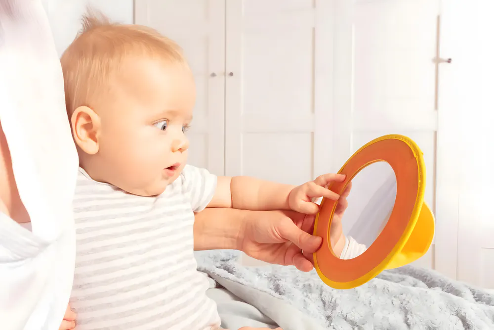 The baby showed curiosity as it looked at its reflection in the mirror