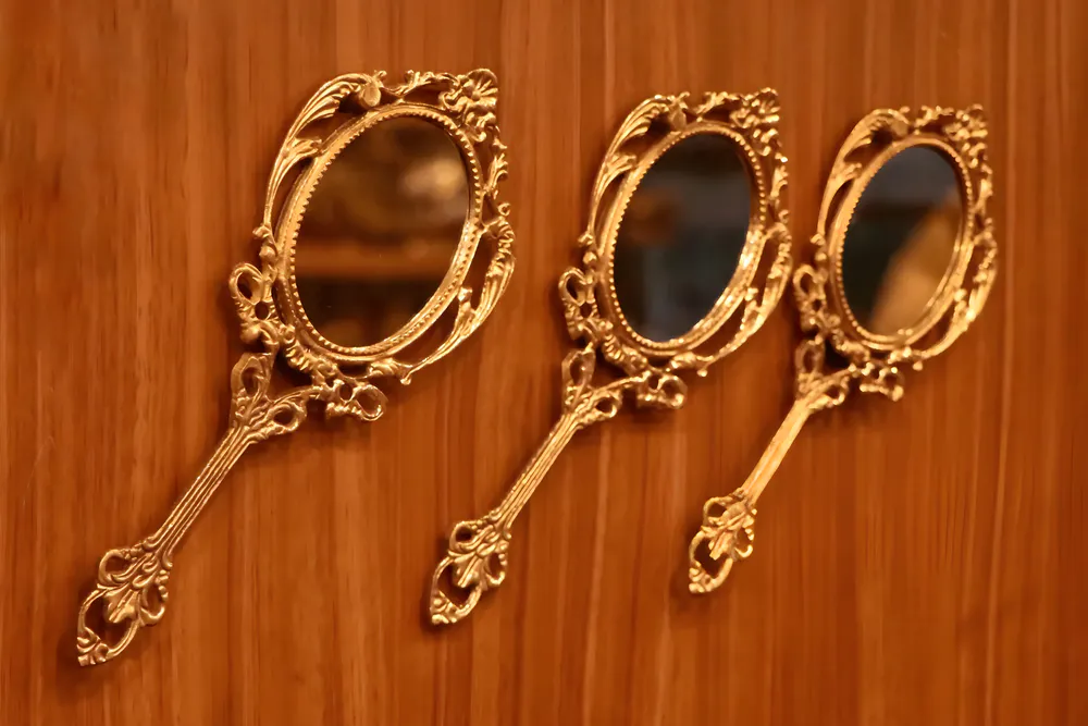 Three identical hand mirrors are hanging on a wooden wall