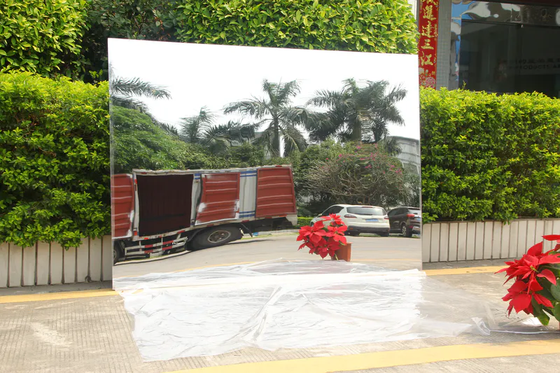 The large acrylic mirror leans against the edge of the flower bed (uneven).